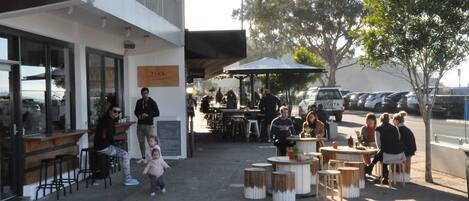 Un café en plein air avec des tables et des chaises, un espace de repos abrité et une enseigne indiquant un restaurant.