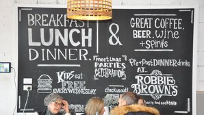 Eine Schiefertafel mit Werbung für Frühstück, Mittagessen, Abendessen und Getränke nach dem Abendessen in einem Restaurant.