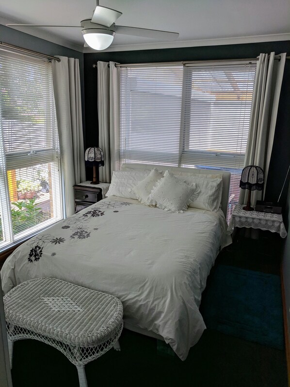 A bedroom with a bed, a small white chair, a nightstand, and a ceiling fan. - Eliza Stays" Getaway. (Mount Eliza)