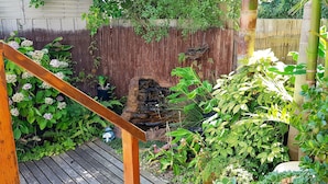 A wooden deck with a bamboo fence, lush greenery, and a small waterfall feature. -  Eliza Stays" Getaway. (Mount Eliza)