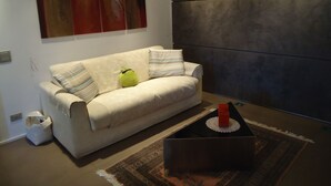 Un soggiorno moderno con un divano, cuscini, un piccolo peluche verde, un tavolino da caffè con un oggetto rosso e un tappeto decorato.