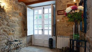 A stone-walled entrance with a white door, a bicycle, a radiator, and a vase with flowers.