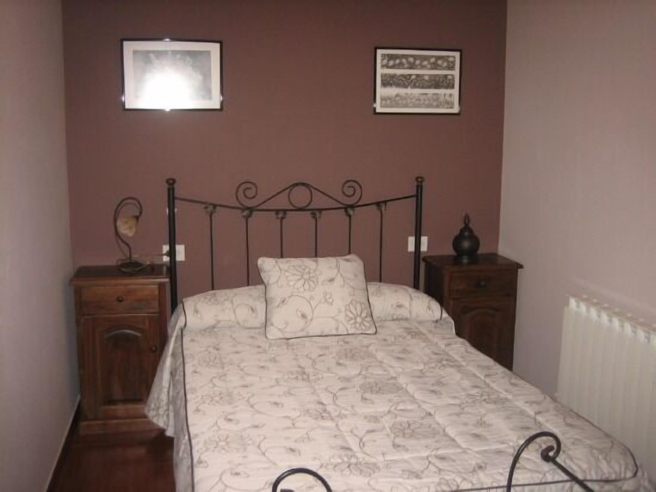 Un dormitorio con una cama, una mesita de noche, un aparador y dos cuadros en la pared.