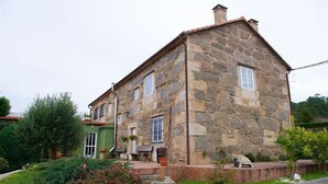 A stone house with a green door, a small porch, and a garden with bushes and a tree.