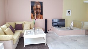 Un soggiorno con un divano beige, un tavolino da caffè bianco, una TV a schermo piatto e un vaso decorativo.
