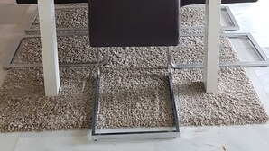 Un'area pranzo con un tavolo bianco, sedie nere, uno specchio decorativo e un vaso con piante secche.