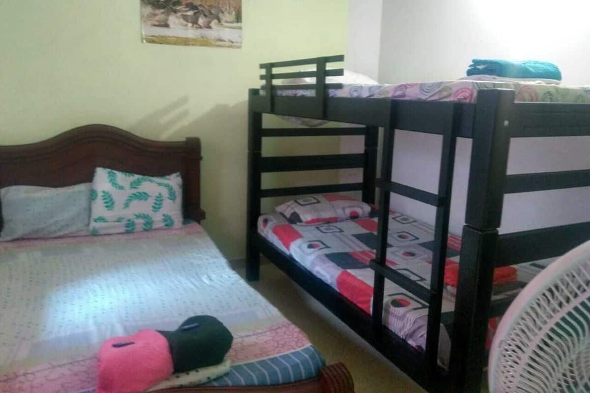A room with two bunk beds, a wooden headboard, a bed with a patterned bedspread, and a wall-mounted fan.
