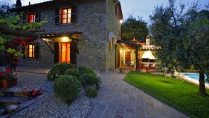 A stone house with a well-lit entrance, a pool, and a garden with potted plants. - Villa immersed in the nature, relax and privacy, private pool and garden (Castiglion Fiorentino)