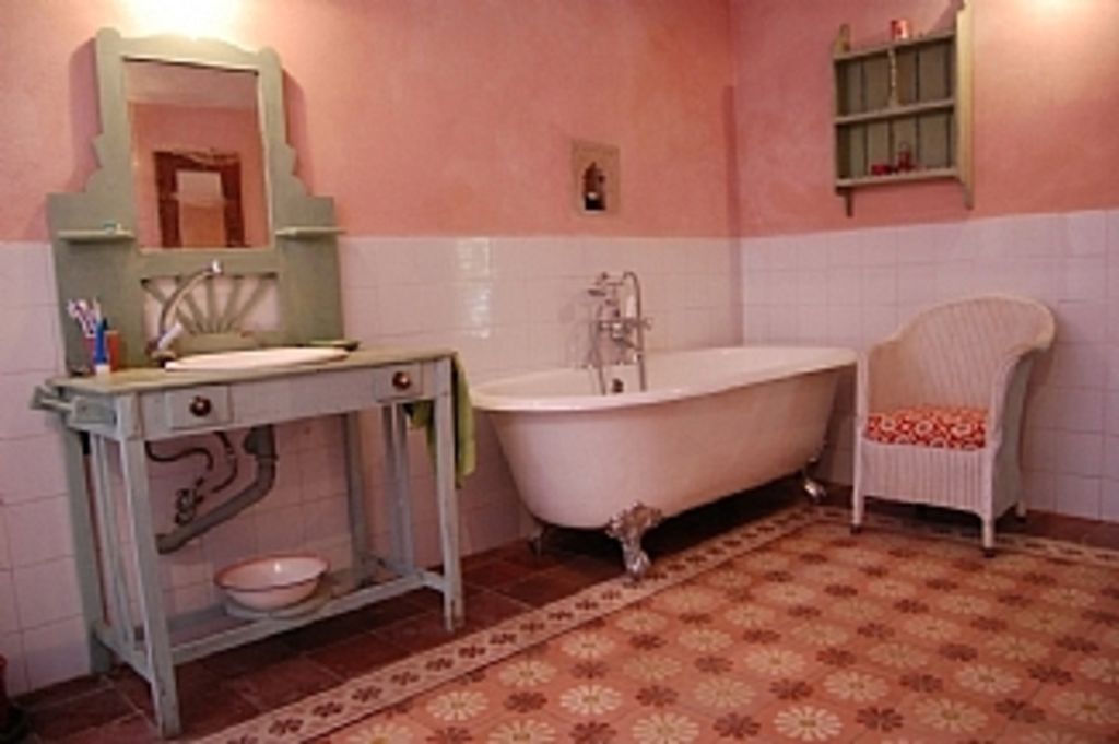 Un baño con una bañera independiente, un lavamanos con espejo y una silla.