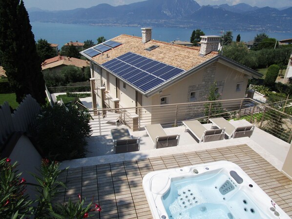 Una casa con paneles solares en la azotea, un jacuzzi y vistas a un lago y montañas.