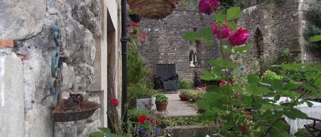 A rustic stone building with a garden area featuring potted plants and flowers.