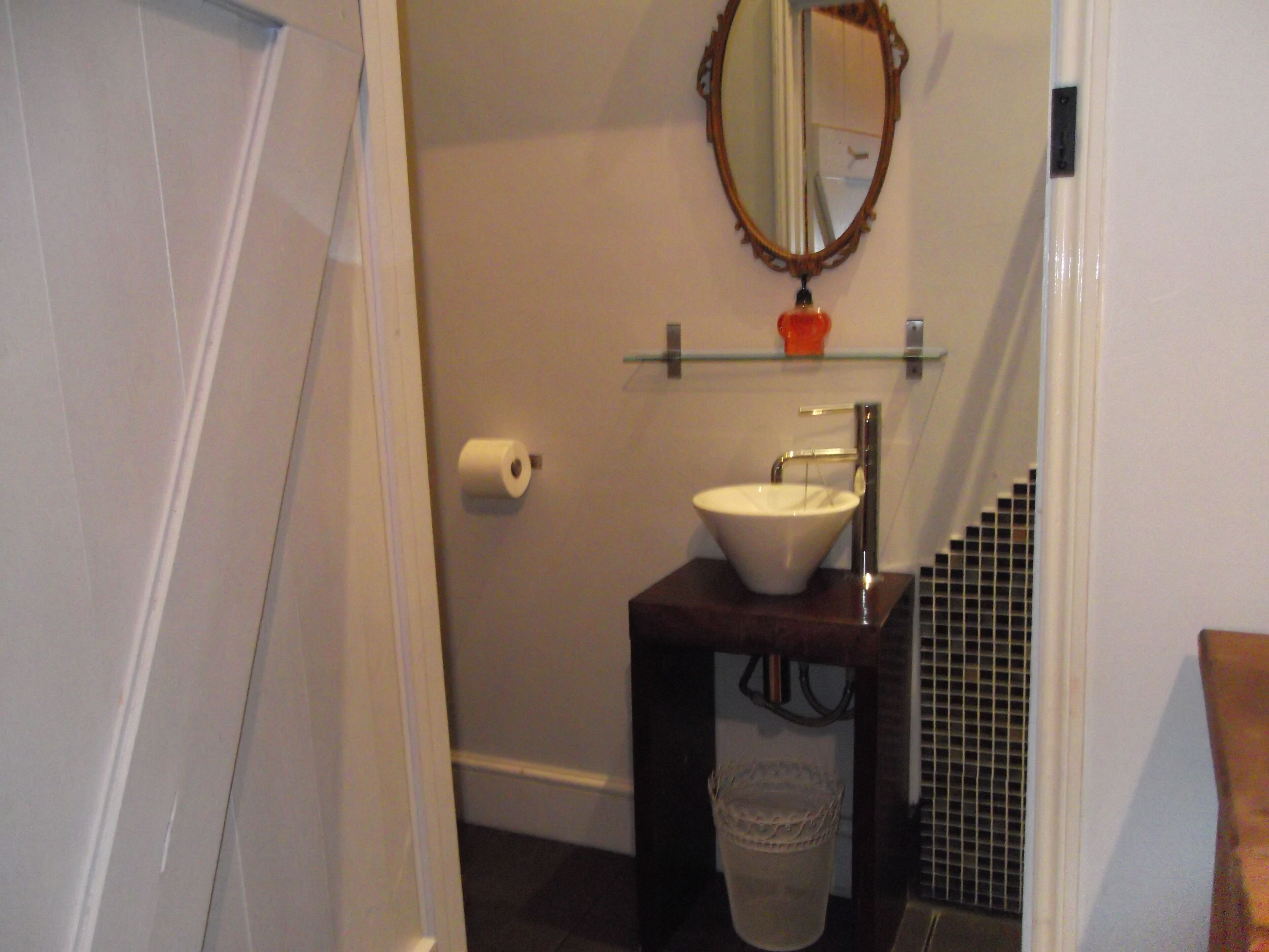 A bathroom with a white sink, a mirror, a roll of toilet paper, and a trash can.