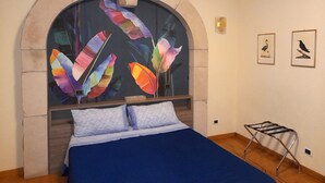 Quarto com cama grande, cabeceira em arco e obra de arte na parede com penas coloridas.