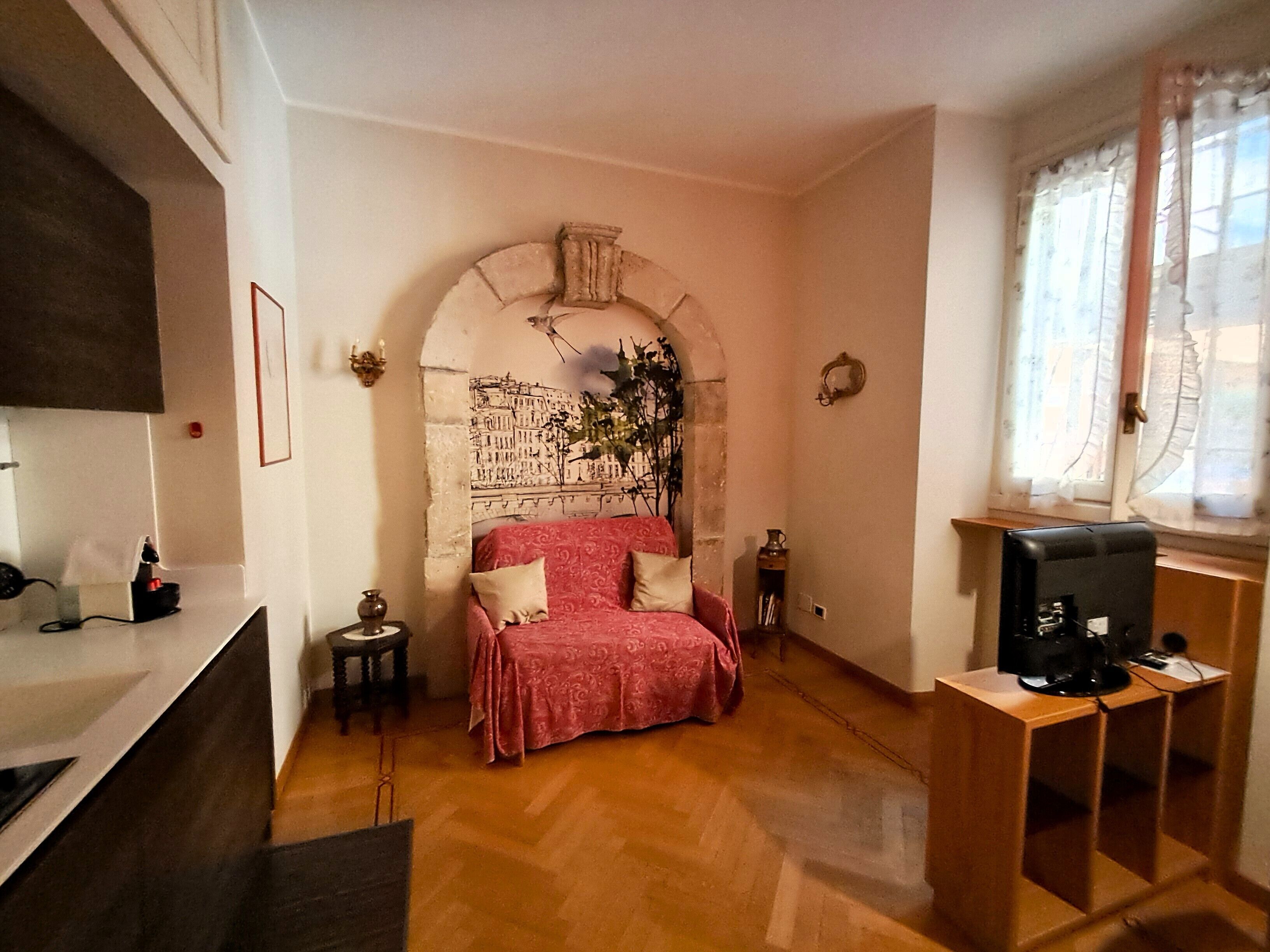 Une chambre à coucher comprenant un lit, un téléviseur, une fenêtre avec des rideaux et un mur agrémenté d’une arche décorative.
