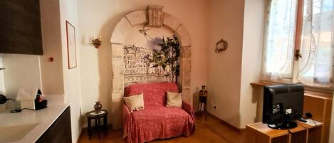 A bedroom with a bed, a television, a window with curtains, and a wall with a decorative arch.