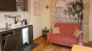 Uma sala de estar acolhedora com uma kitchenette, um sofá com estofamento estampado e uma parede decorativa com um mural de paisagem urbana.