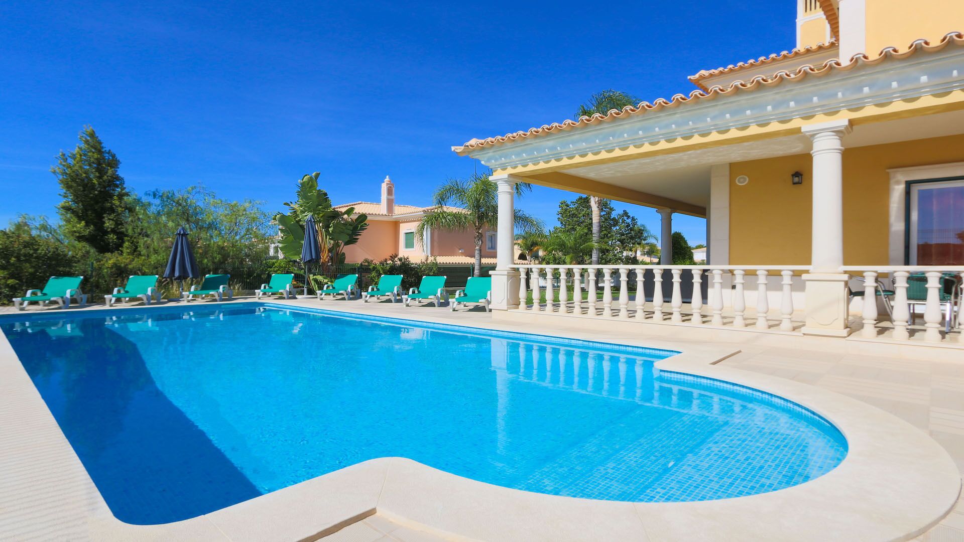 A swimming pool with lounge chairs and a covered area with columns.
