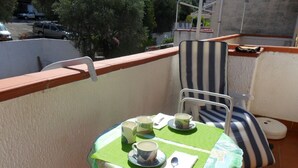 A small balcony with a table set for two, a striped chair, and a view of parked cars and trees. - Diamond holiday 2019 La Casa Di Fra  (Diamante)