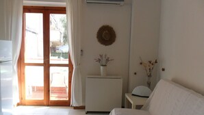A hotel room with a bed, a small table with a vase, an air conditioning unit, and a view through the door. - Diamond holiday 2019 La Casa Di Fra  (Diamante)