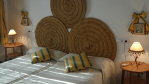 Een net opgemaakt bed met gestreepte kussens, een rond geweven wanddecoratie en twee bedlampjes.