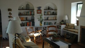 Een gezellige woonkamer met een bank, stoelen, een tafel, boekenkasten, een open haard en een lamp.