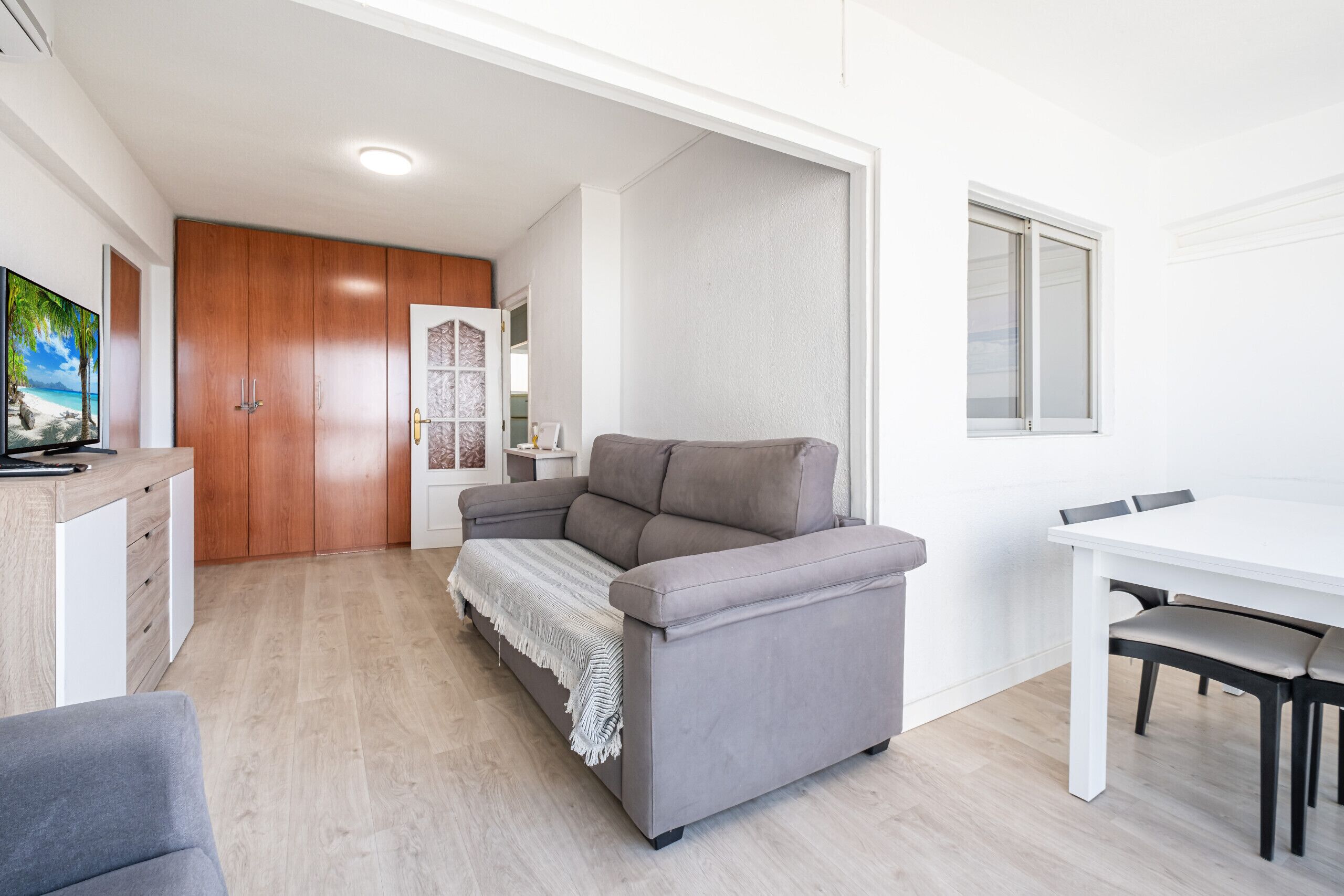 A compact living space with a grey sofa, a dining table, and a TV on a wooden cabinet.