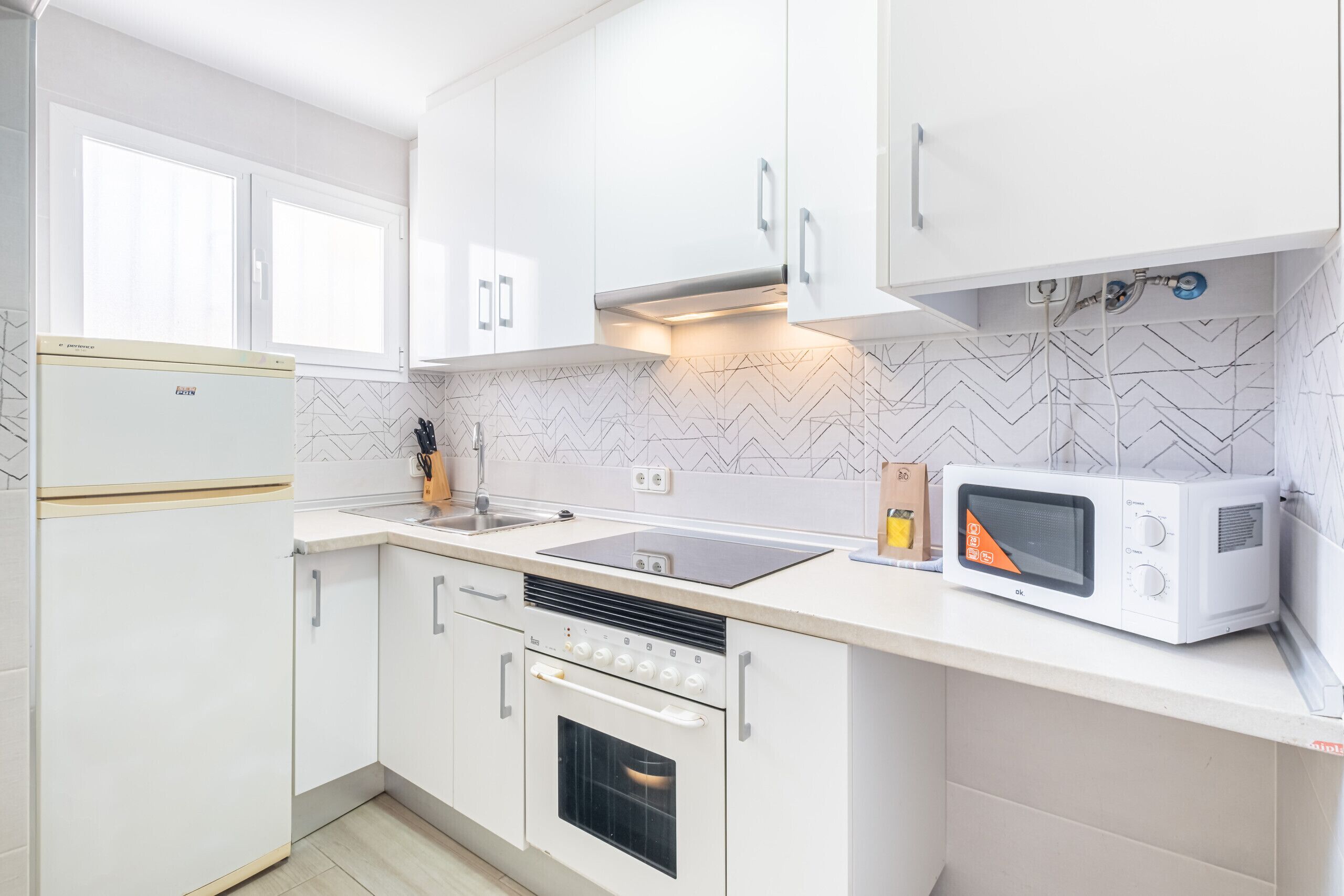 Een moderne keuken met witte kasten, een ingebouwde oven, een magnetron en een gasfornuis.