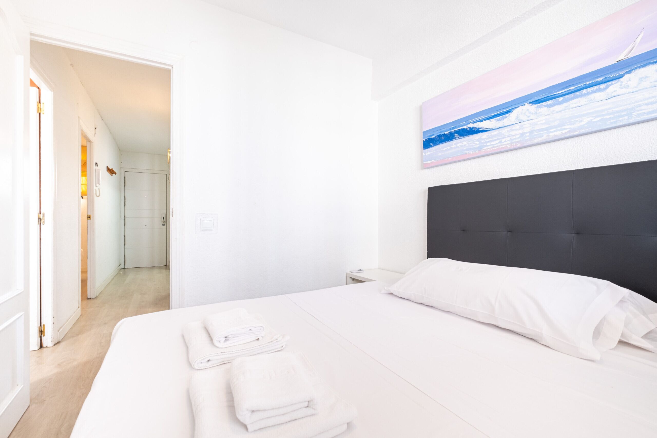 A hotel room with a large bed, a nightstand, a painting on the wall, and a door leading to another room.