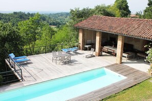 Ein Poolbereich mit Liegestühlen und Grillplatz, umgeben von einer Holzterrasse und Blick ins Grüne.
