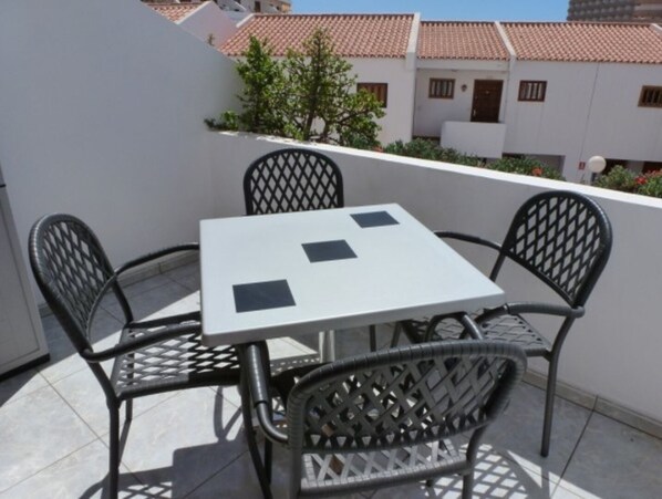 A balcony with a white table and four wicker chairs.