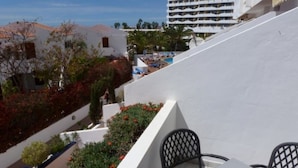 A white building with a sloped roof, a patio with a table and chairs, and a view of other buildings and greenery in the background.