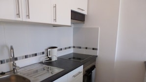A kitchen with white cabinets, a black countertop, a stainless steel sink, and a microwave.