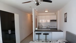 A compact living space with a kitchenette, a bed with a floral-patterned bedspread, and a ceiling fan.