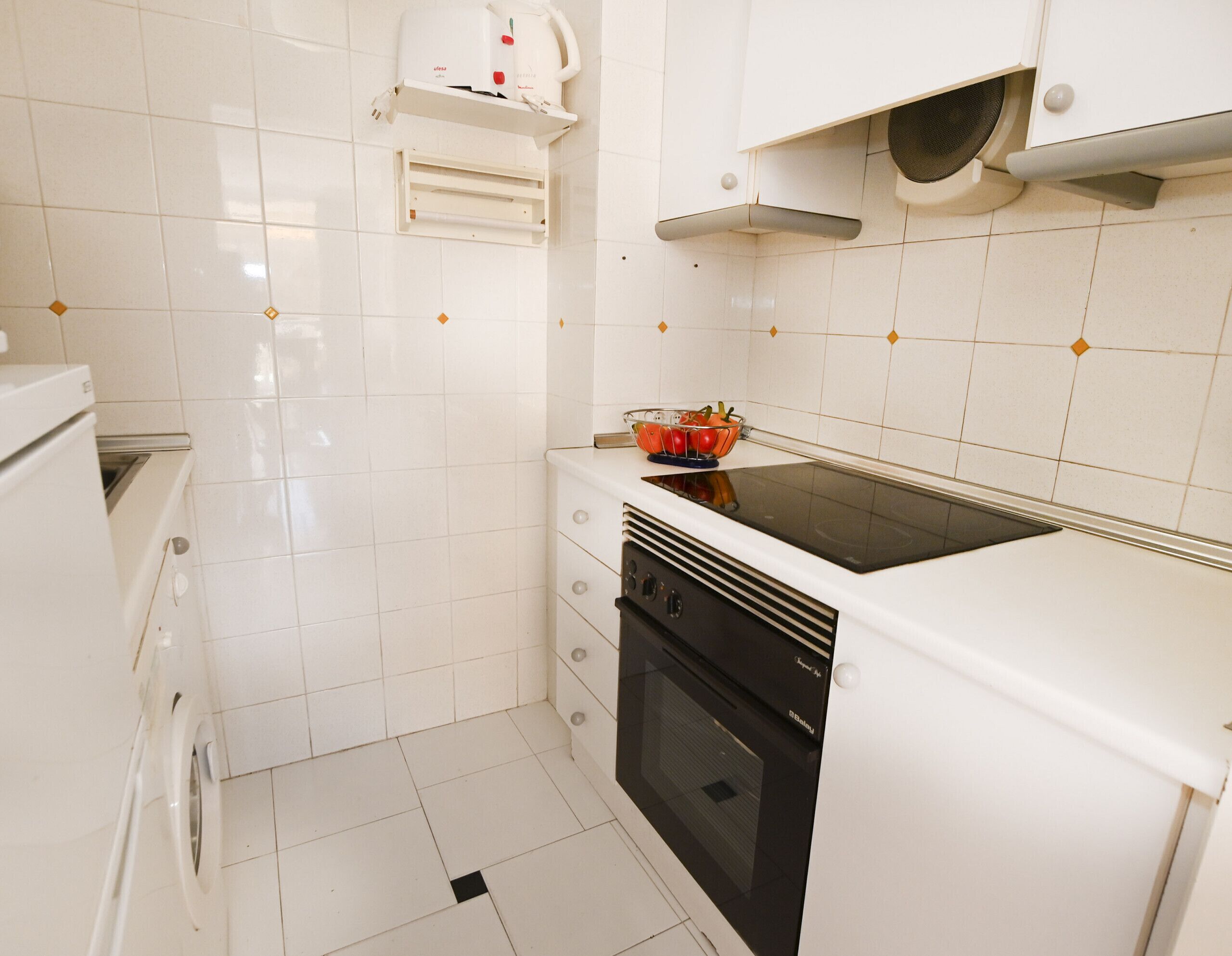 Cocina compacta con muebles blancos, estufa negra y una pequeña encimera.