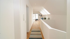 Een modern interieur met een houten vloer, een gestreept tapijt en een trap naar een balkon met planten.