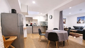A modern kitchen with a refrigerator, stove, and sink; a dining area with a table and chairs; a living room with a sofa and a rug; and a kitchen island.