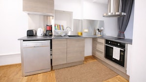 A modern kitchen with stainless steel appliances, wooden cabinets, a built-in dishwasher, and a range hood.
