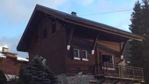 Una cabaña de madera con base de piedra, un balcón y un paisaje cubierto de nieve.