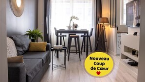 A modern living room with a grey sofa, a dining table with chairs, a floor lamp, and a TV on the right. - SUPERB Appt DRC lorient center fully EQUIPPED  (Lorient)