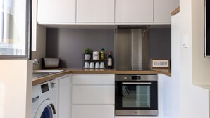 A compact kitchen with a washing machine, oven, and a shelf with kitchen essentials. - SUPERB Appt DRC lorient center fully EQUIPPED  (Lorient)