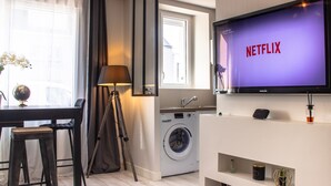 A modern living room with a flat-screen TV displaying 'NETFLIX', a washing machine, a dining table with chairs, and a lamp. - SUPERB Appt DRC lorient center fully EQUIPPED  (Lorient)