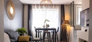 Una sala de estar moderna con un sofá gris, una mesa de comedor con sillas, una lámpara de pie y un televisor a la derecha.