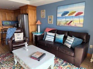 A living room with a brown leather sofa, a white coffee table, and a colorful rug. - Most Amazing Views ever in this beautiful 2 bedrm 2 bath condo in Resort area! (Tybee Island)
