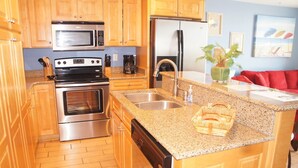 Una cocina con armarios de madera, electrodomésticos de acero inoxidable, encimeras de granito, un fregadero y un sofá rojo en la zona de estar contigua.