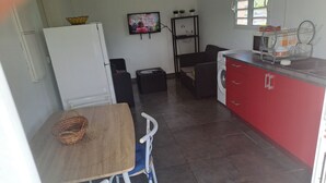 A compact kitchen with a dining area, a washing machine, and a TV on the wall. - Damencourt bungalows Section Damencourt chemin de pinadiere 97160 le mold  (guadeloupe)