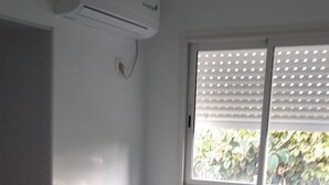 A bedroom with a bed, a wardrobe, an air conditioner, and a window with blinds. - Damencourt bungalows Section Damencourt chemin de pinadiere 97160 le mold  (guadeloupe)