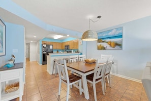 A modern kitchen with a central island, white cabinetry, and a dining area with a wooden table and chairs.
