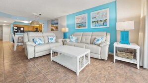 A living room with a white sofa set, a coffee table, and a blue wall with paintings. - Near Main St., Oceanfront, 6th Floor, Pools, Wifi | AshWorth - 602 (North Myrtle Beach)