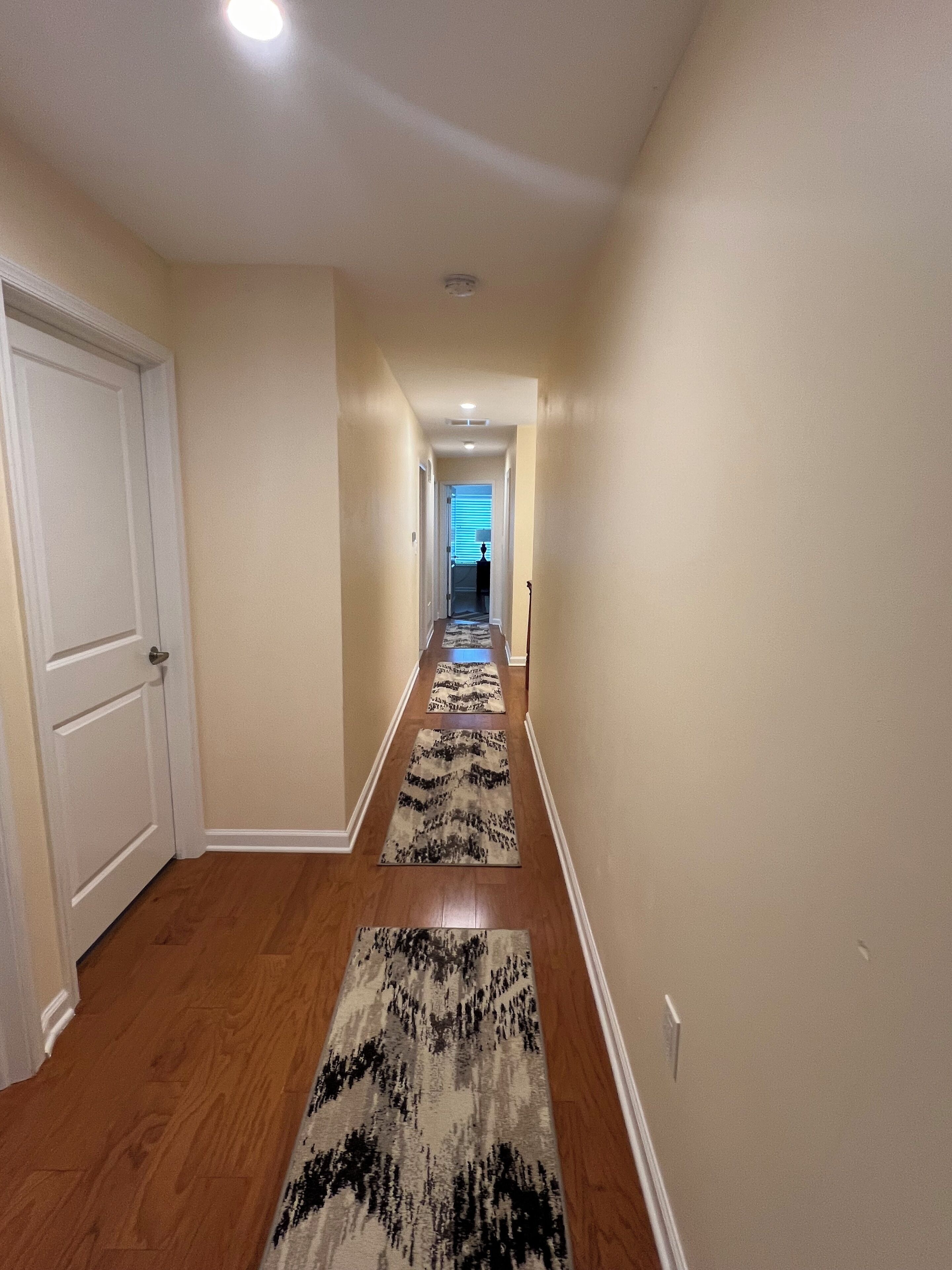 Un pasillo con pisos de madera, paredes color beige y alfombras estampadas.