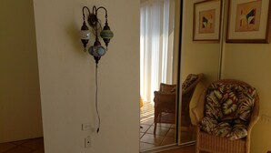 A room with a white wall, a mirror reflecting a chair and a window, and a wall-mounted light fixture. - The Cottage at Villa Indigo 2BR/1.5BA in Exclusive Private Gated Community (Saint Thomas)